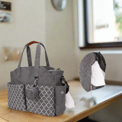 Sac à langer gris avec pochette à lingettes, posé sur une table devant une fenêtre