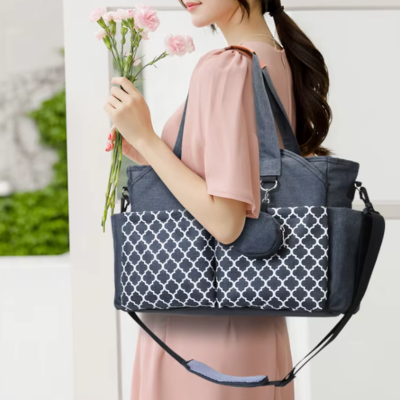 Femme portant un sac à langer gris sur l’épaule et tenant un bouquet de fleurs dans la même main
