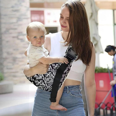 Maman souriante portant  bébé dans une écharpe de portage, assis sur le côté, dans la rue.