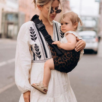 bébé dans echarpe porte bebe leopard porté par maman dans la rue