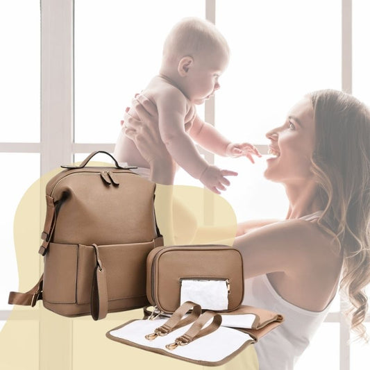 Maman avec son bébé heureux, portant un sac a langer camel équipé de deux crochets pour poussette, d’un matelas à langer et d’une boîte à serviettes.