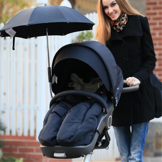 maman pousse poussette avec parapluie et bébé dans nid d'ange installé dan 
