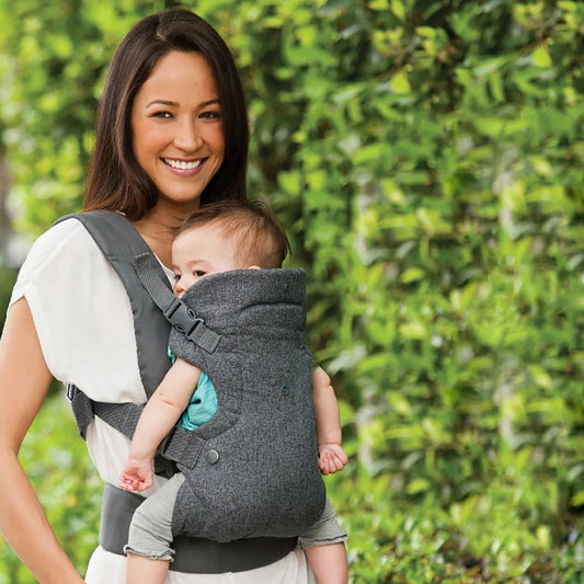 Maman utilise un porte bébé devant un mur d’arbres