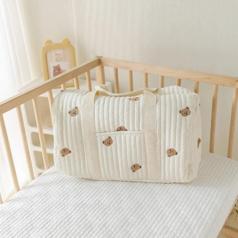 Sac à langer avec motif tête d’ours, déposé sur le matelas d’un lit de bébé à barreaux en bois