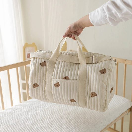 Sac à langer avec motif tête d’ours, tenu d’une main devant un lit de bébé